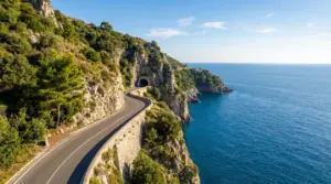 Strada panoramica della Costiera Amalfitana tra scogliere e mare, con curva verso una galleria nella roccia